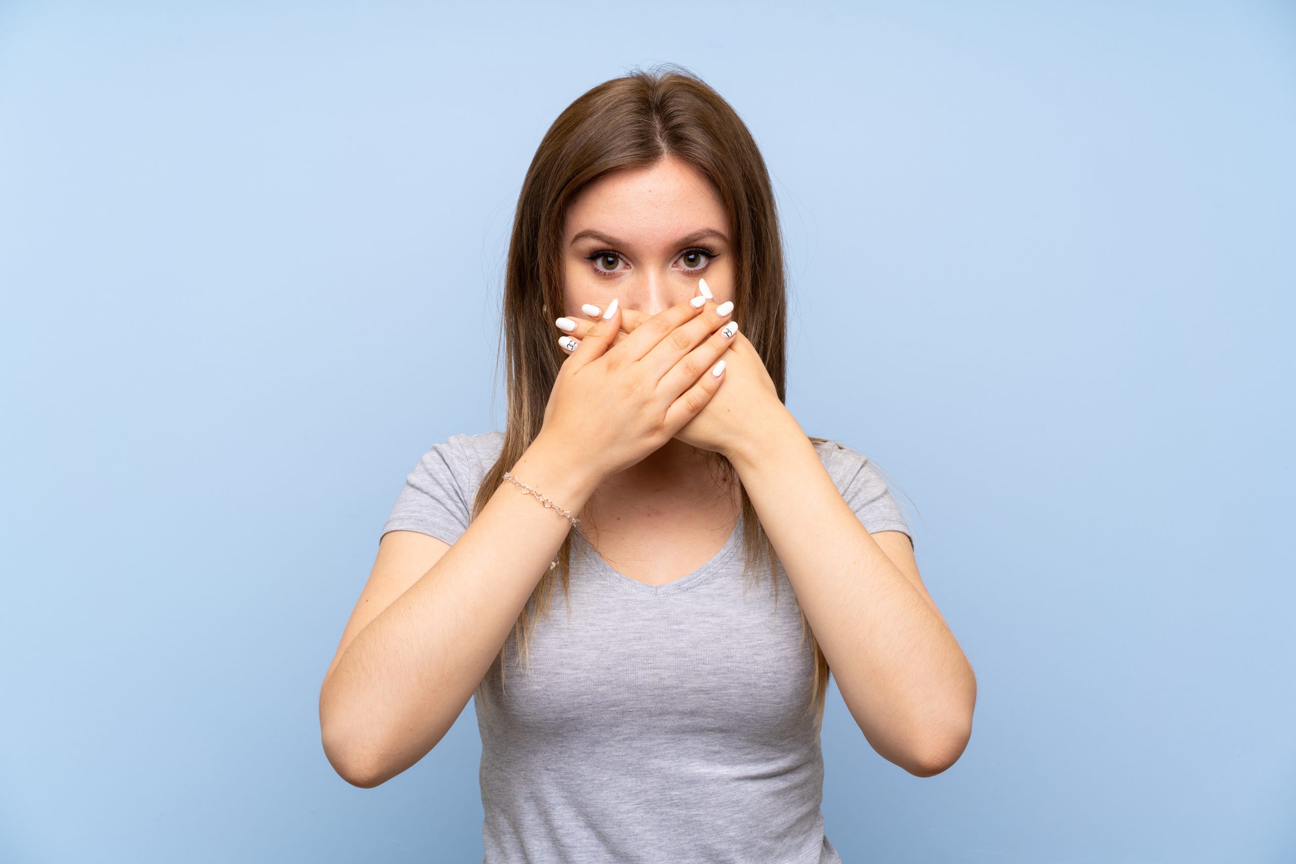 Teenager girl over isolated blue wall covering mouth with hands