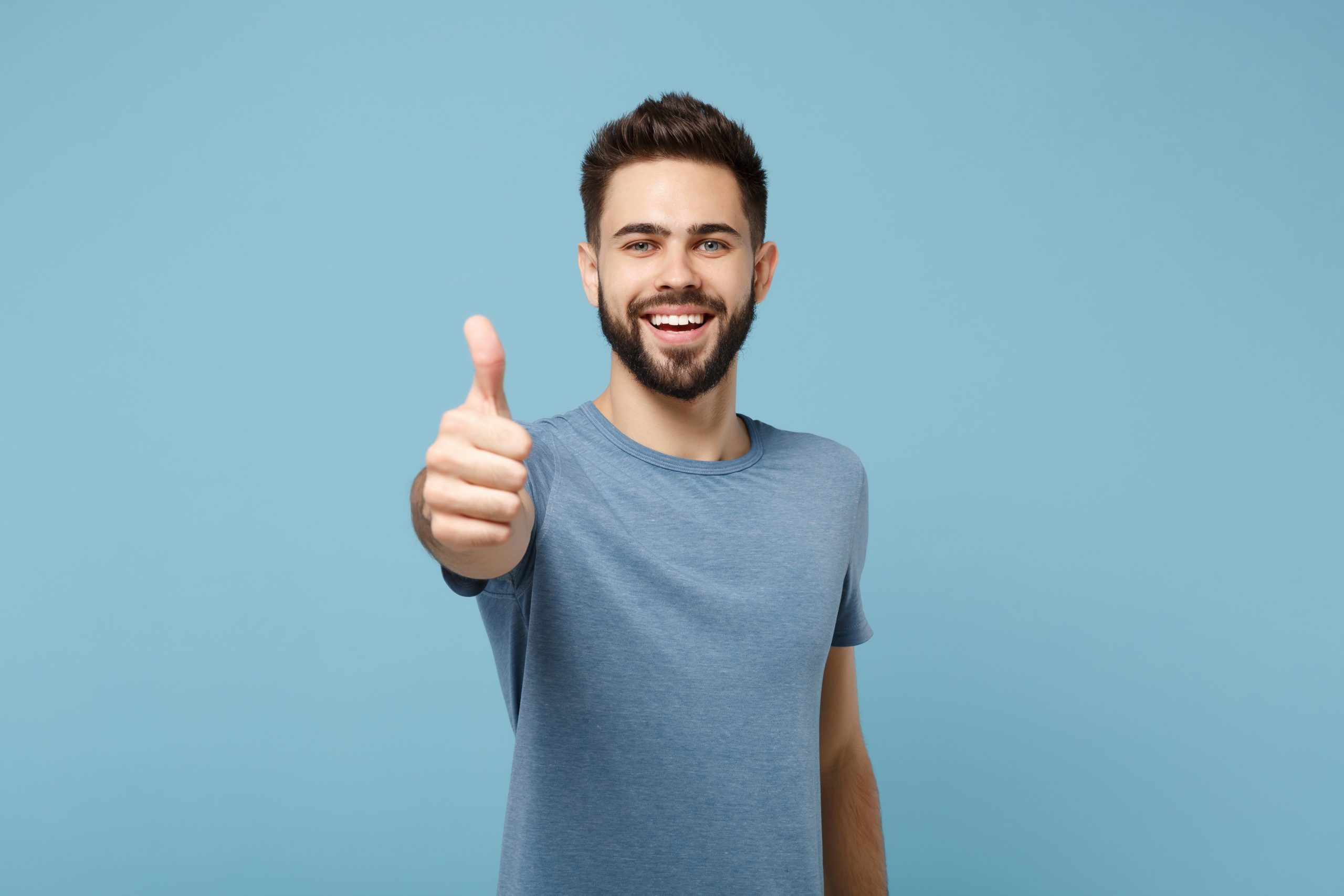 Young smiling cheerful handsome man in casual clothes posing isolated on blue wall background, studio portrait. People sincere emotions lifestyle concept. Mock up copy space. Showing thumb up