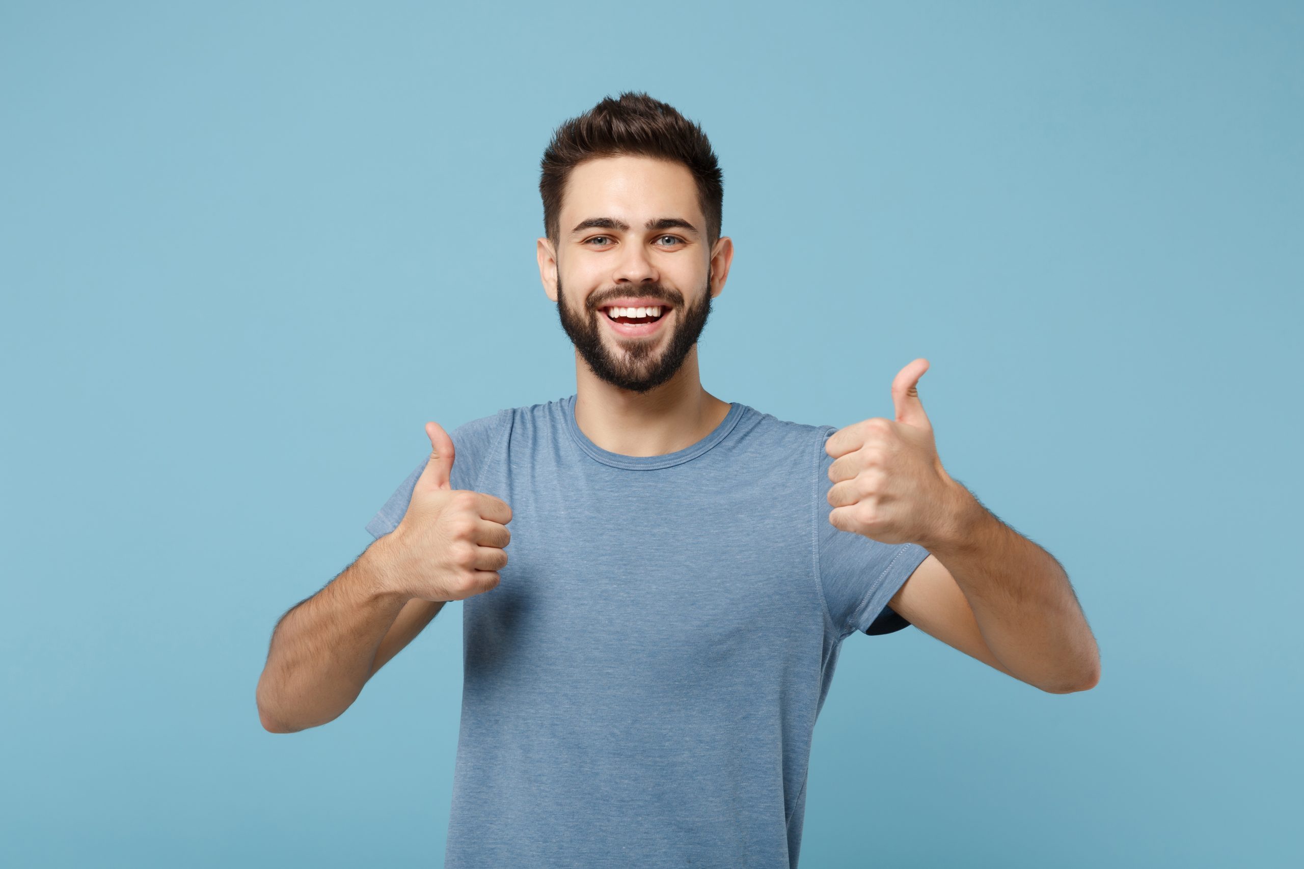 Young joyful funny smiling handsome man in casual clothes posing isolated on blue wall background, studio portrait. People sincere emotions lifestyle concept. Mock up copy space. Showing thumbs up