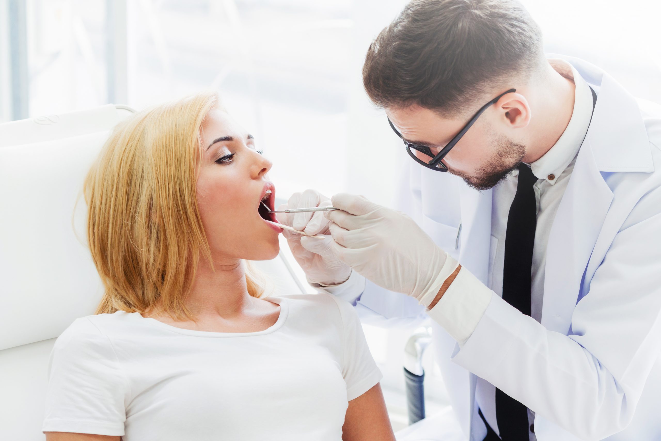 Young handsome dentist examining teeth of happy woman patient sitting on dentist chair in dental clinic. Dentistry care concept.