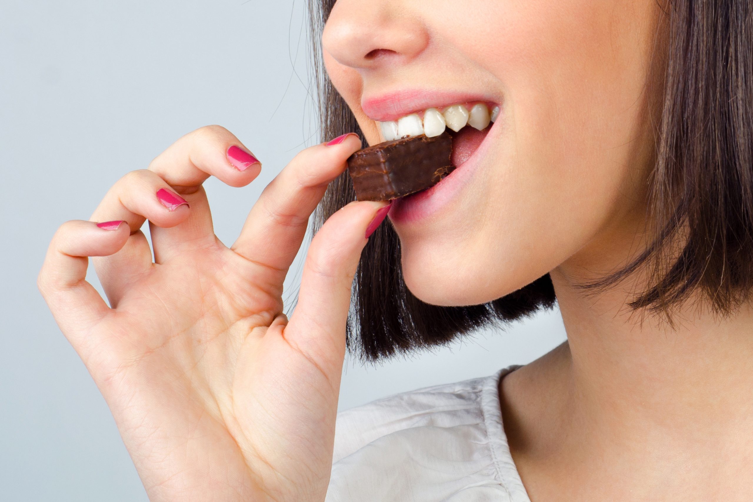 Portrait of the beautiful girl eating chocolate cookies isolated on gray background.