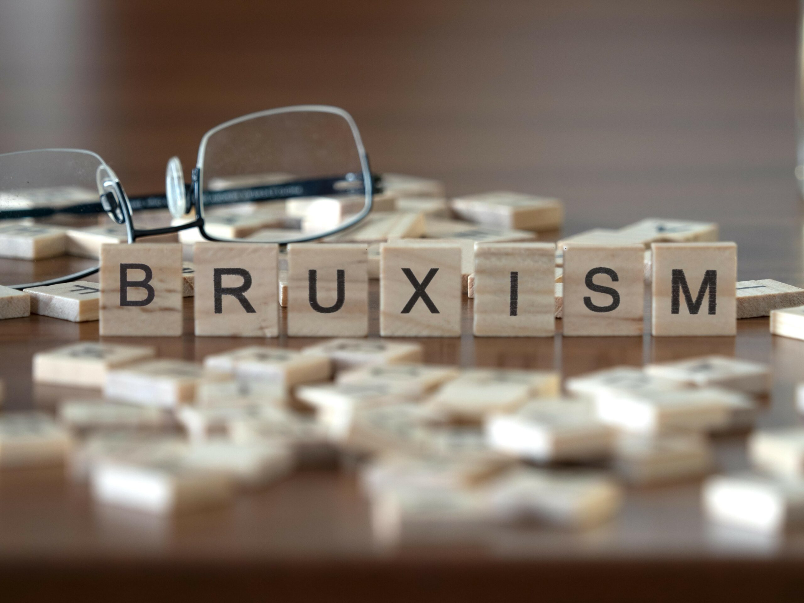 bruxism concept represented by wooden letter tiles on a wooden table with glasses and a book