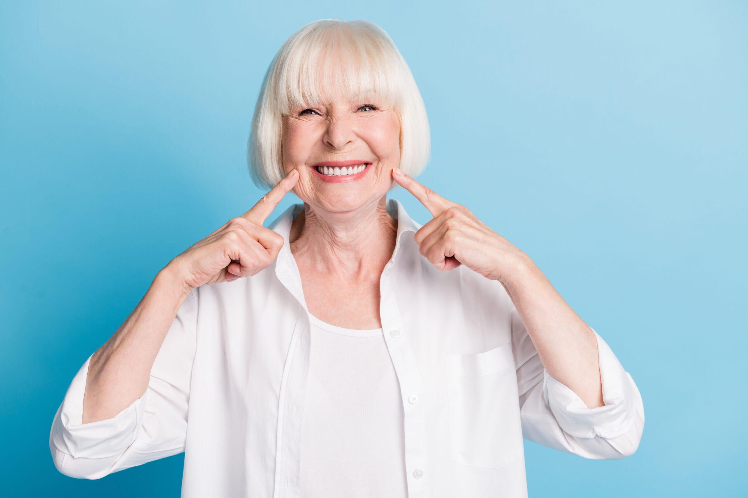 Photo portrait of granny blonde hair pointing at white teeth healthy smile dental whitening veneers isolated on bright blue color background.